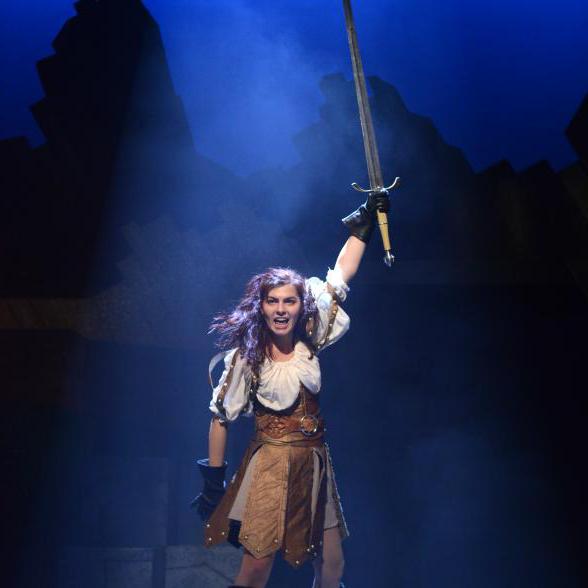 女性站在舞台中央，举着一把剑