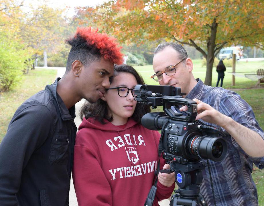 两名学生和一名教授正从一个巨大的摄像机镜头里望过去 